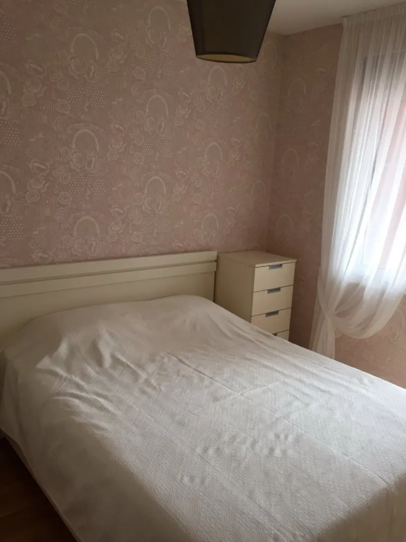 Spavaća soba sa bračnim krevetom, noćnim stočićem i prozorom sa zavjesom.