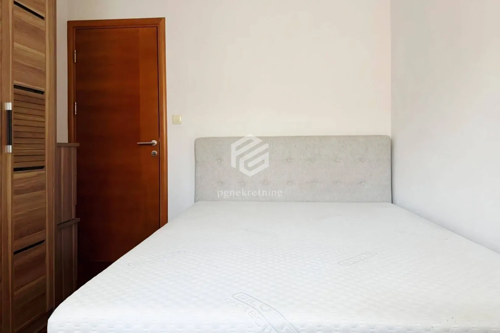 Furnished bedroom with a double bed and a wooden wardrobe.