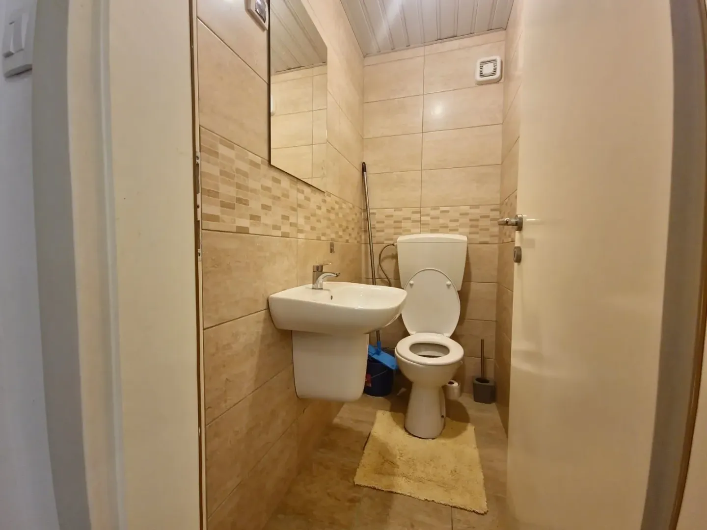 Small bathroom tiled in beige with a sink and toilet.