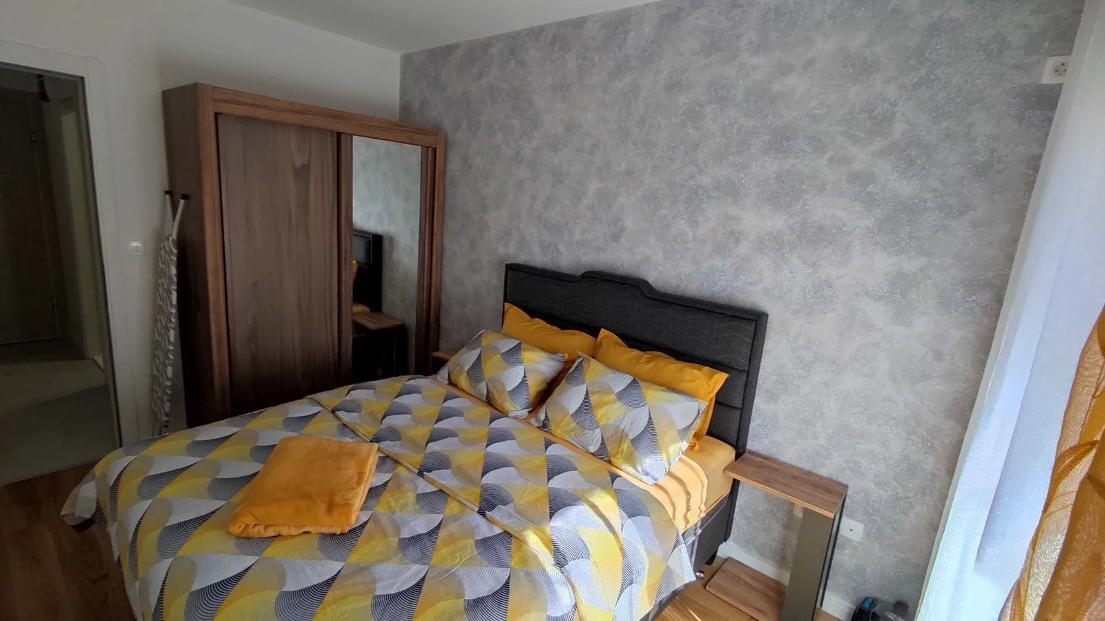 Furnished bedroom with a double bed and a wooden wardrobe.