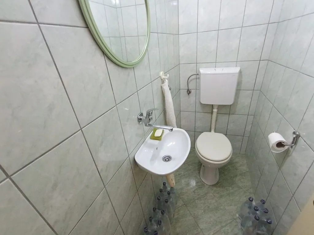 Manje kupatilo sa umivaonikom, WC šoljom i zidnim pločicama.