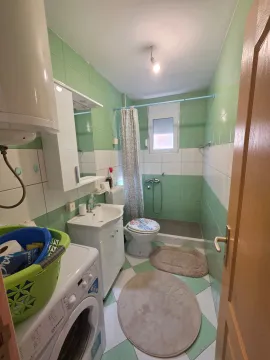 Small bathroom with green and white tiles, sink, toilet, and washing machine. - image 13