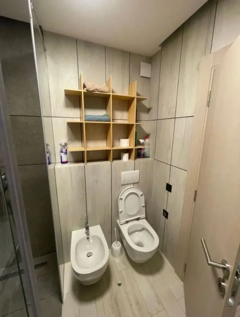 Moderno opremljeno kupatilo sa sanitarijama i drvenim zidnim policama.