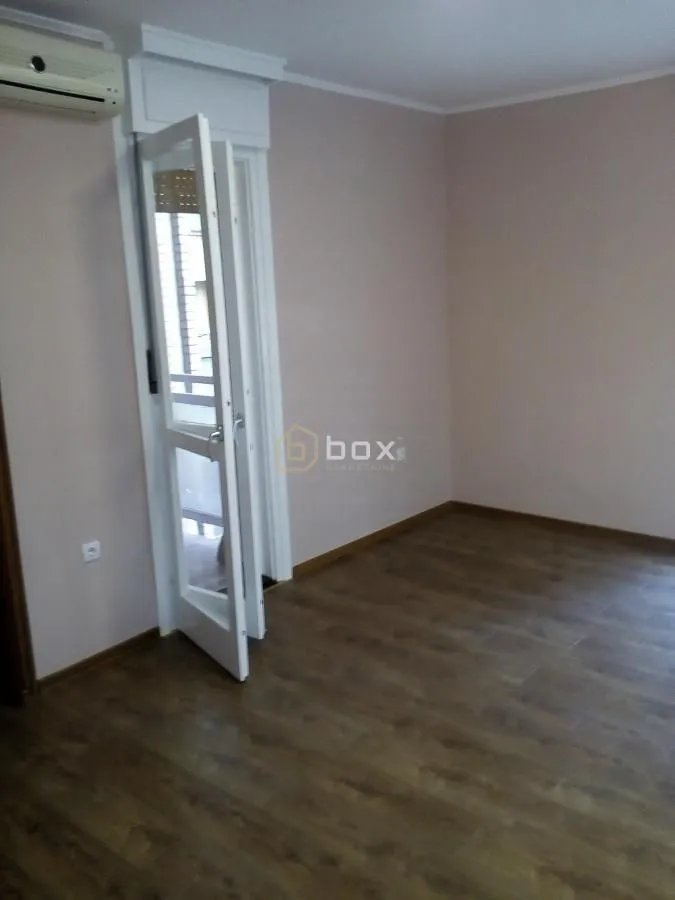Empty room with wooden flooring and balcony doors.