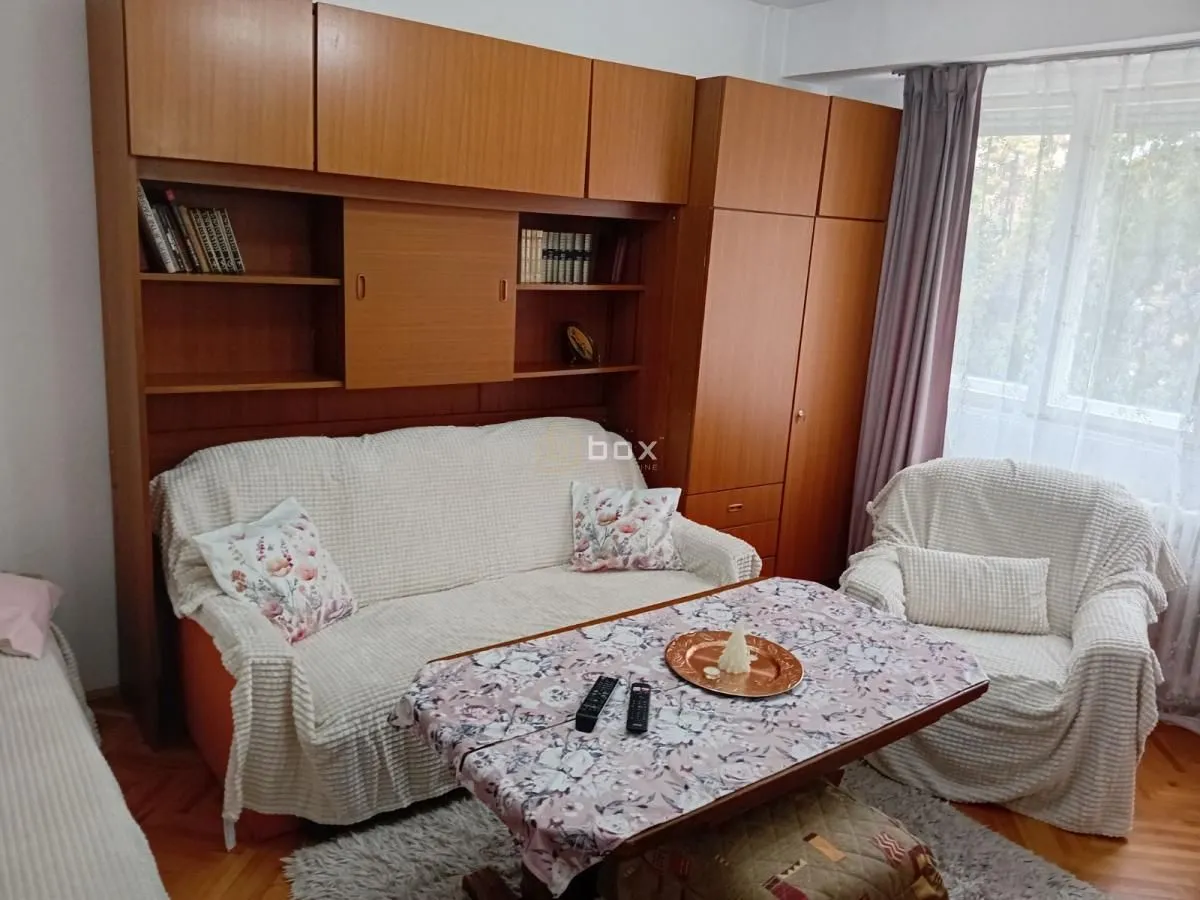 Dnevna soba sa garniturom za sedenje, stočićem i drvenim ormarima.