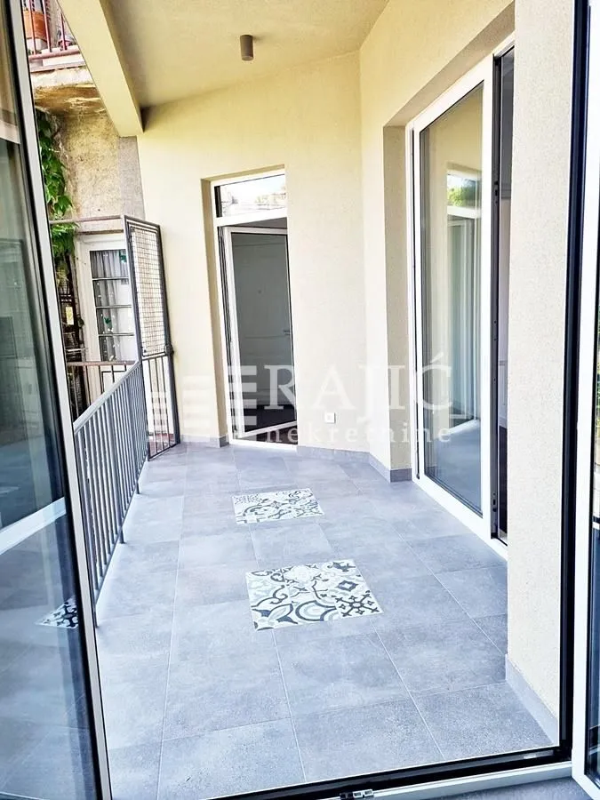 Spacious tiled terrace with metal railing and large balcony doors.