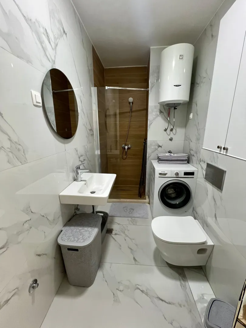 Moderne kupatilo sa tuš kabinom, umivaonikom i veš mašinom.