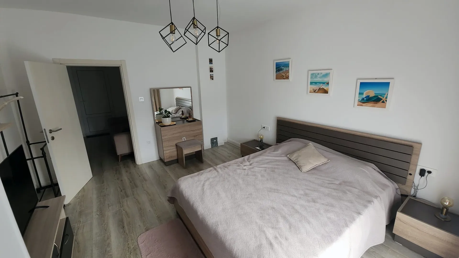 Prostrana spavaća soba sa bračnim krevetom, komodom i modernim lusterima.