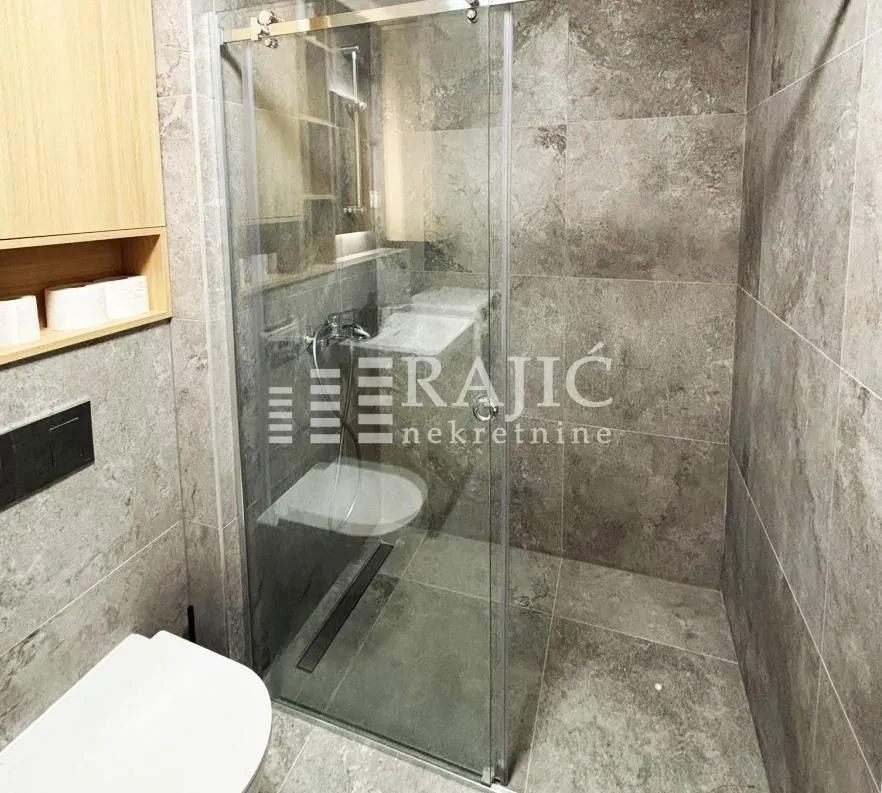 Modern bathroom with a walk-in shower and grey tiled walls.