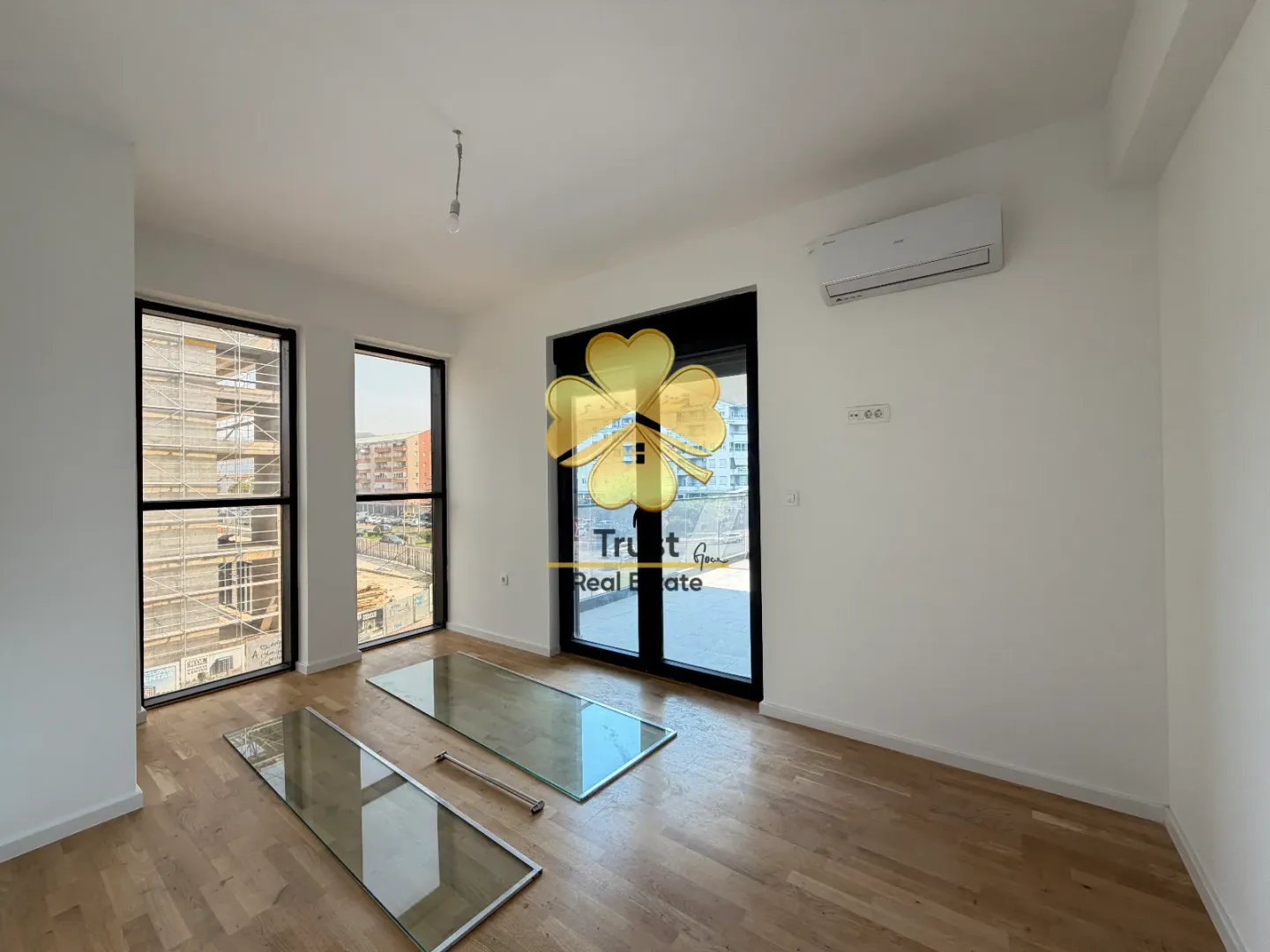 Empty room with hardwood floors, large windows, and an air conditioning unit.