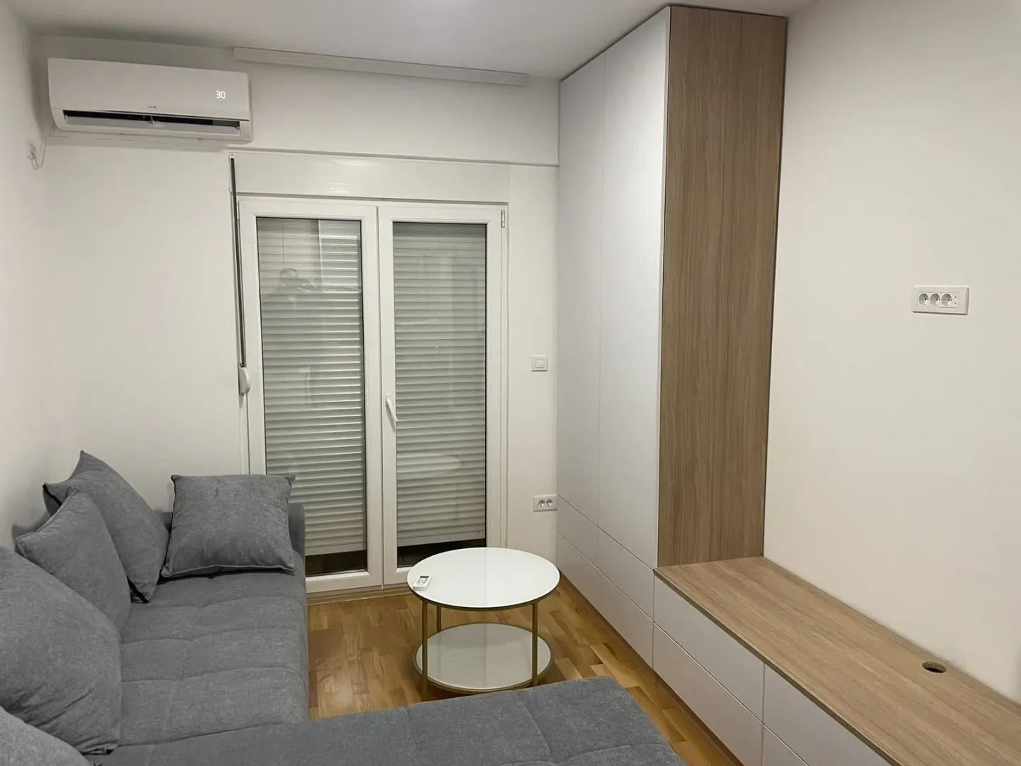 Svijetla dnevna soba sa sivom garniturom i ugradnim namještajem.