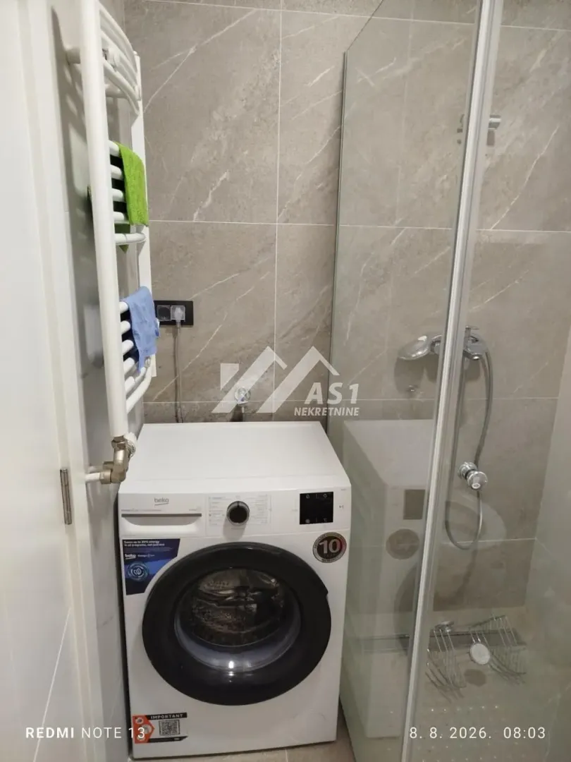 Kupatilo sa tuš kabinom, mašinom za veš i radijatorom za peškire.