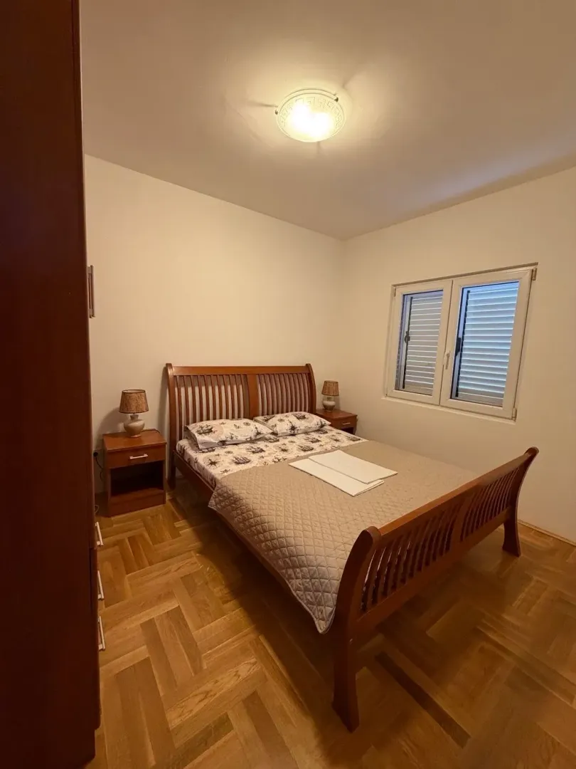 Namještena spavaća soba sa bračnim krevetom, parketom i prozorom.
