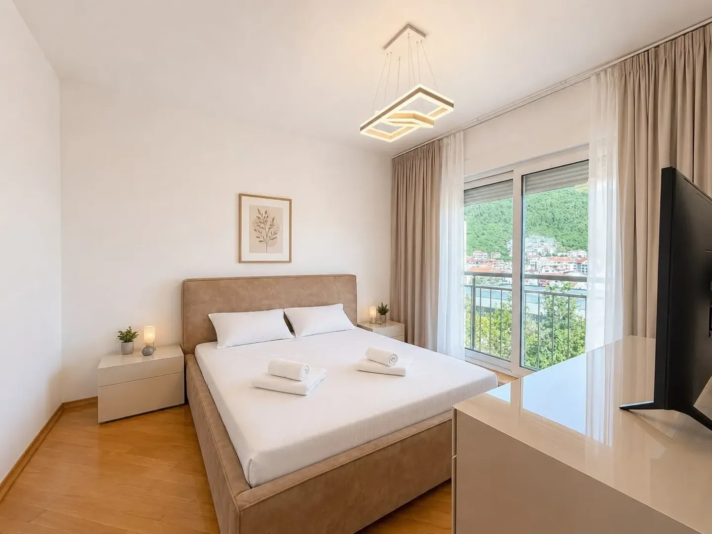 Bright bedroom with a double bed, TV, and access to a balcony with a view.