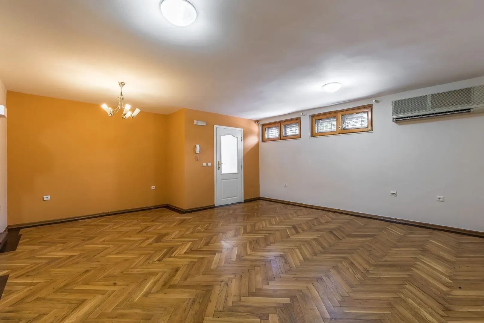 An empty spacious room with parquet flooring and an orange wall.