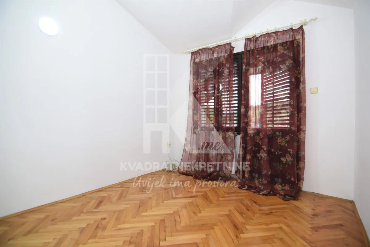 Empty room with parquet flooring and a window with dark red curtains.