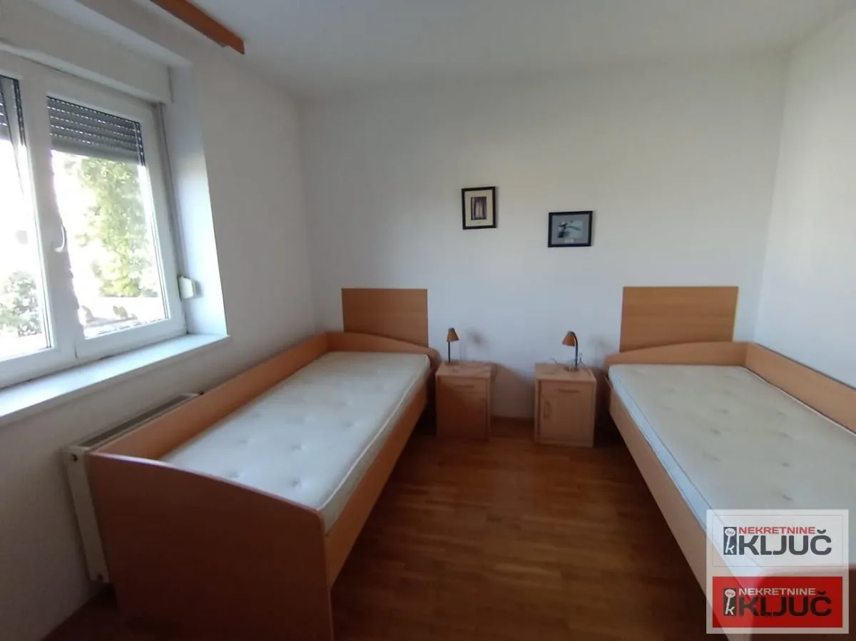 Spavaća soba sa dva drvena kreveta i noćnim stočićima.