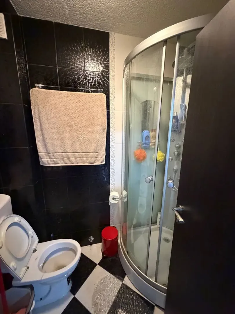 Manje kupatilo sa tuš kabinom, WC šoljom i crno-bijelim pločicama na podu.