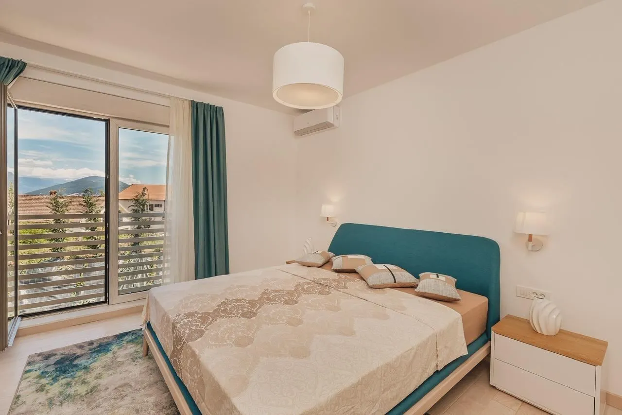 Svijetla spavaća soba sa plavim uzglavljem i izlazom na balkon.
