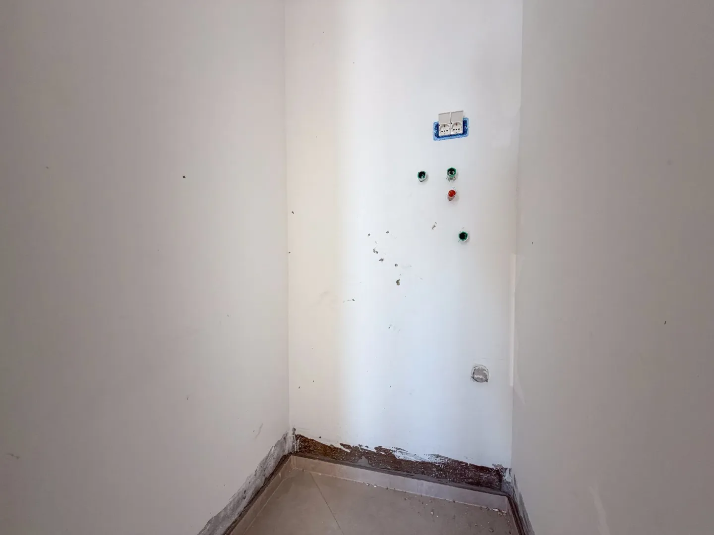 Prazan dio prostorije sa priključcima na bijelom zidu i keramičkim pločicama na podu.