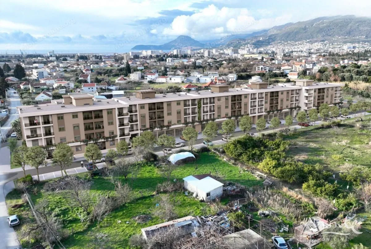 Pogled iz vazduha na novu stambenu zgradu sa okolnim naseljem i planinama u pozadini.