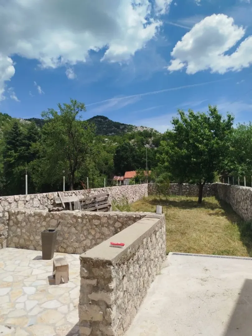 Dvorište sa kamenim zidom i pogledom na planinu.