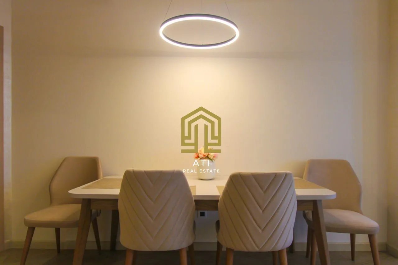 Trpezarija sa stolom, stolicama i modernim visecim lusterom.