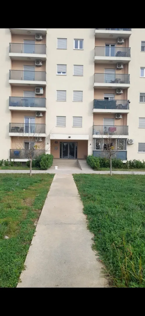 Ulaz u stambenu zgradu sa betonskom stazom i travnjakom.