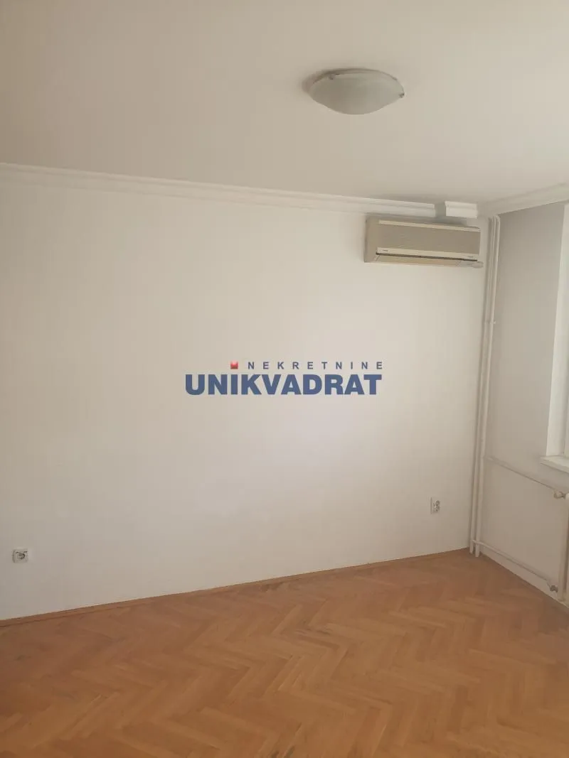 Prazna soba sa parketom i klima uređajem na zidu.
