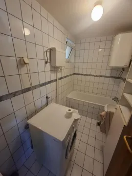Kupatilo obloženo belim pločicama sa kadom i veš mašinom. - image 10