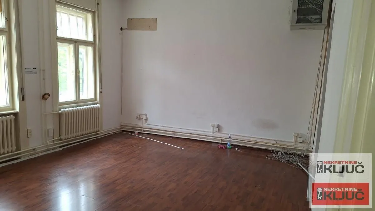 Prazna soba sa drvenim podom i prozorima.