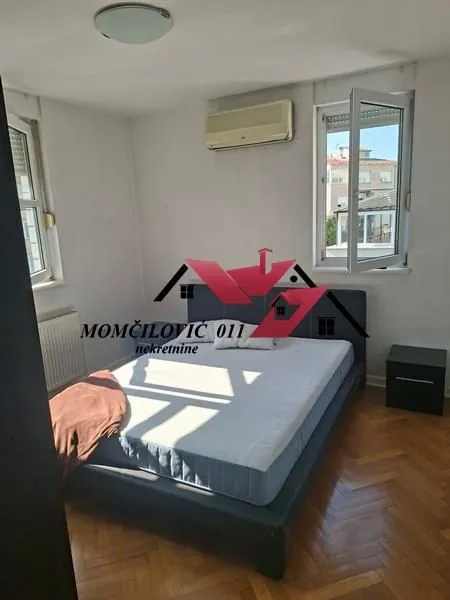 Spavaća soba sa bračnim krevetom, noćnim stočićem i dva prozora.