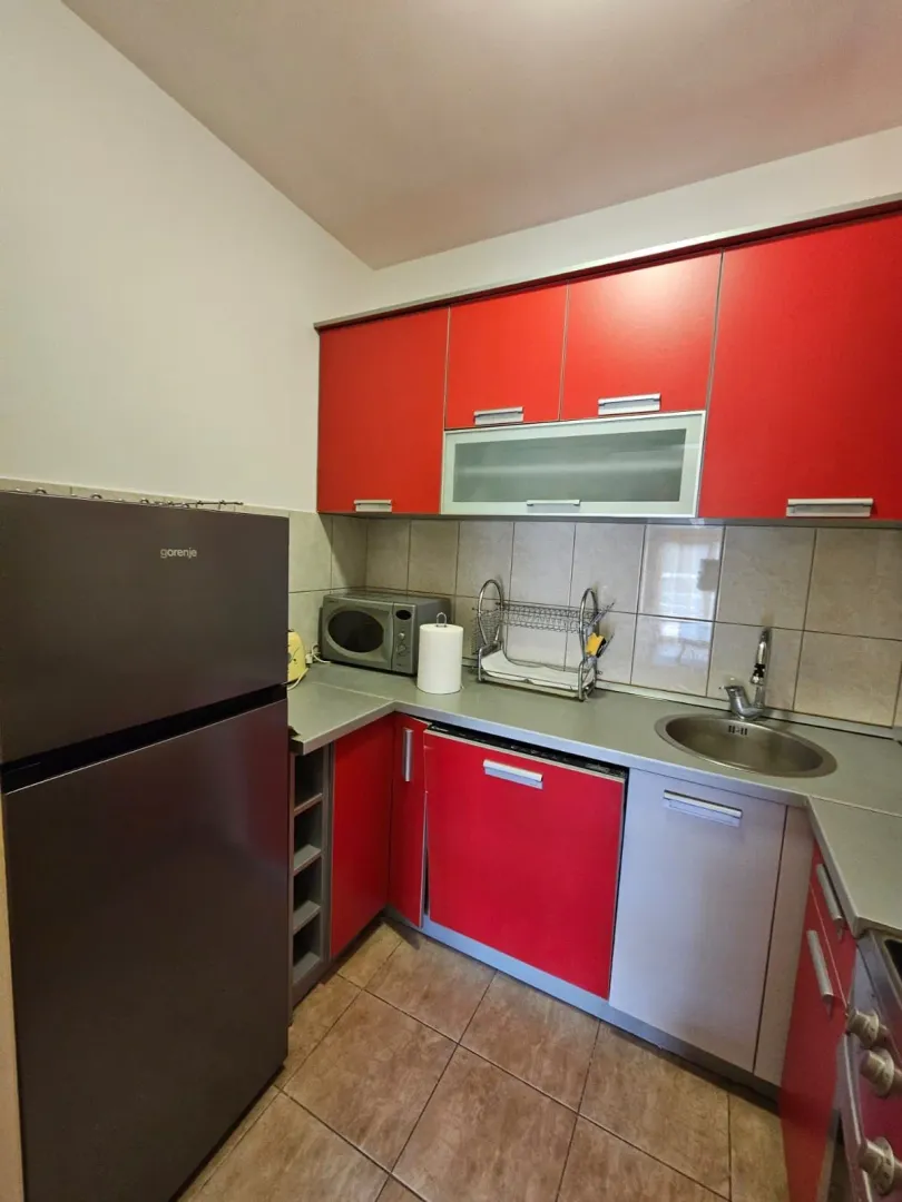 Manja kuhinja sa crvenim elementima i frižiderom.