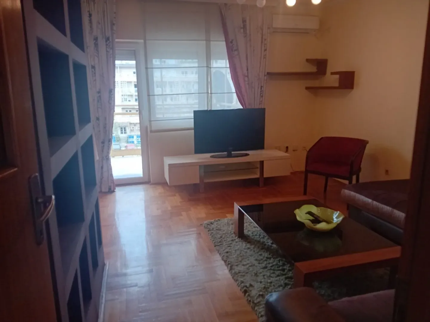 Svijetla dnevna soba sa televizorom, klub stolom i izlazom na terasu.
