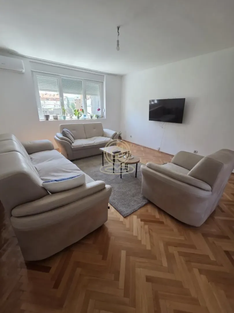 Dnevna soba sa garniturom za sedenje, stočićima i televizorom na zidu.