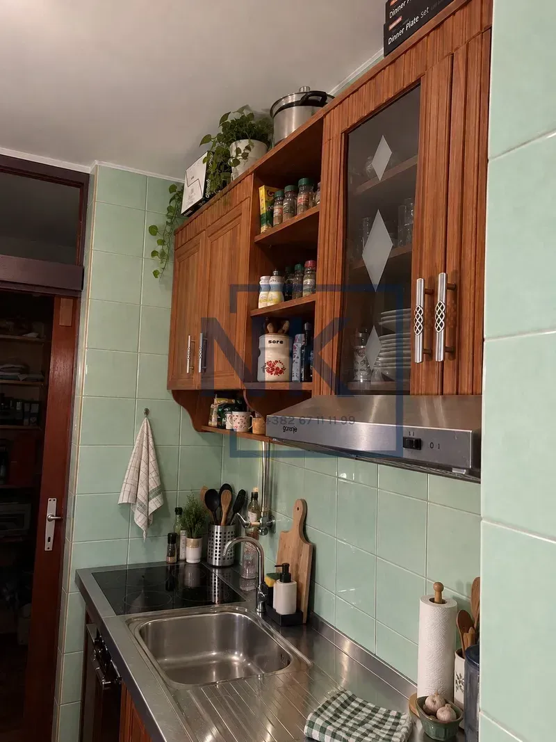 Manja kuhinja sa drvenim visećim elementima i zelenim zidnim pločicama.
