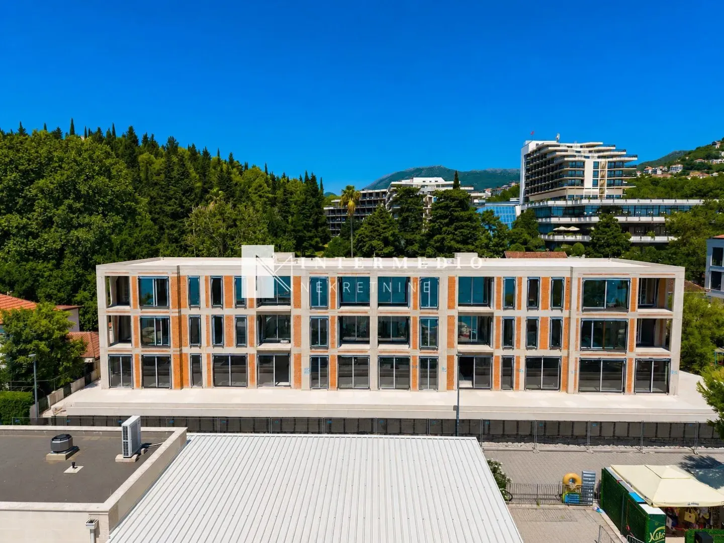 Pogled iz vazduha na fasadu stambene zgrade u izgradnji okružene zelenilom.