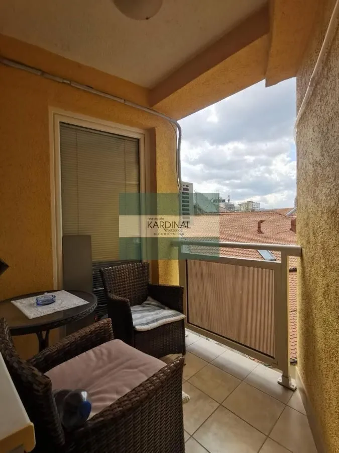Natkriveni balkon sa garniturom za sedenje i pogledom na okolne krovove.