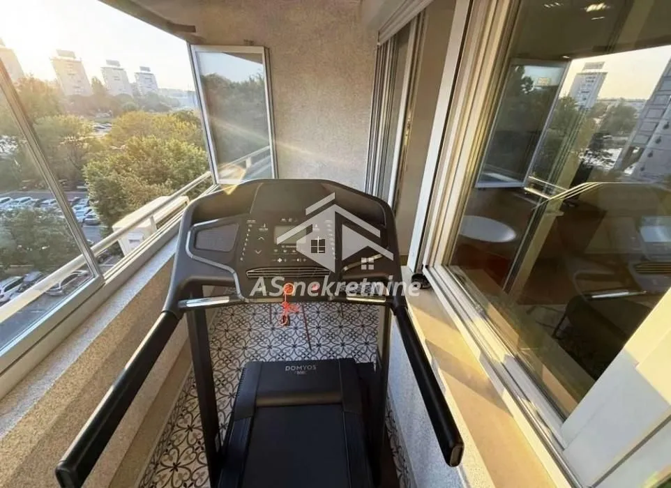 Zastakljeni balkon sa trakom za trčanje i pogledom na okolinu.