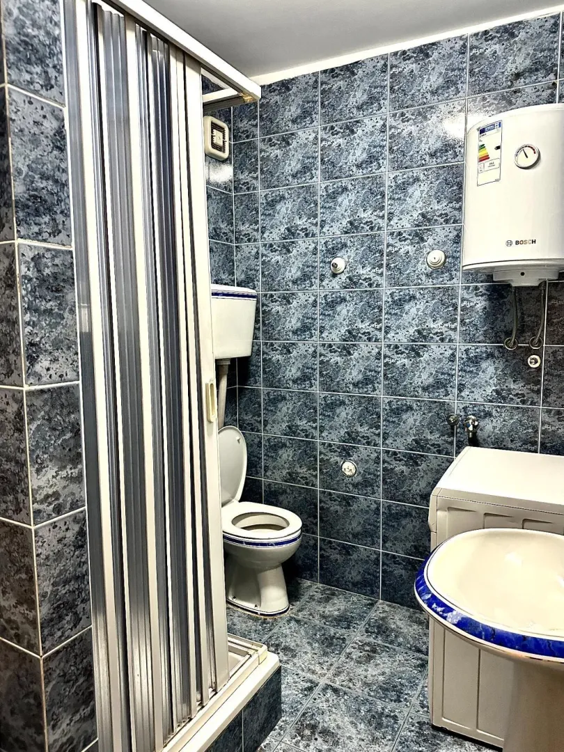 Kupatilo sa plavim pločicama, tuš kabinom i veš mašinom.