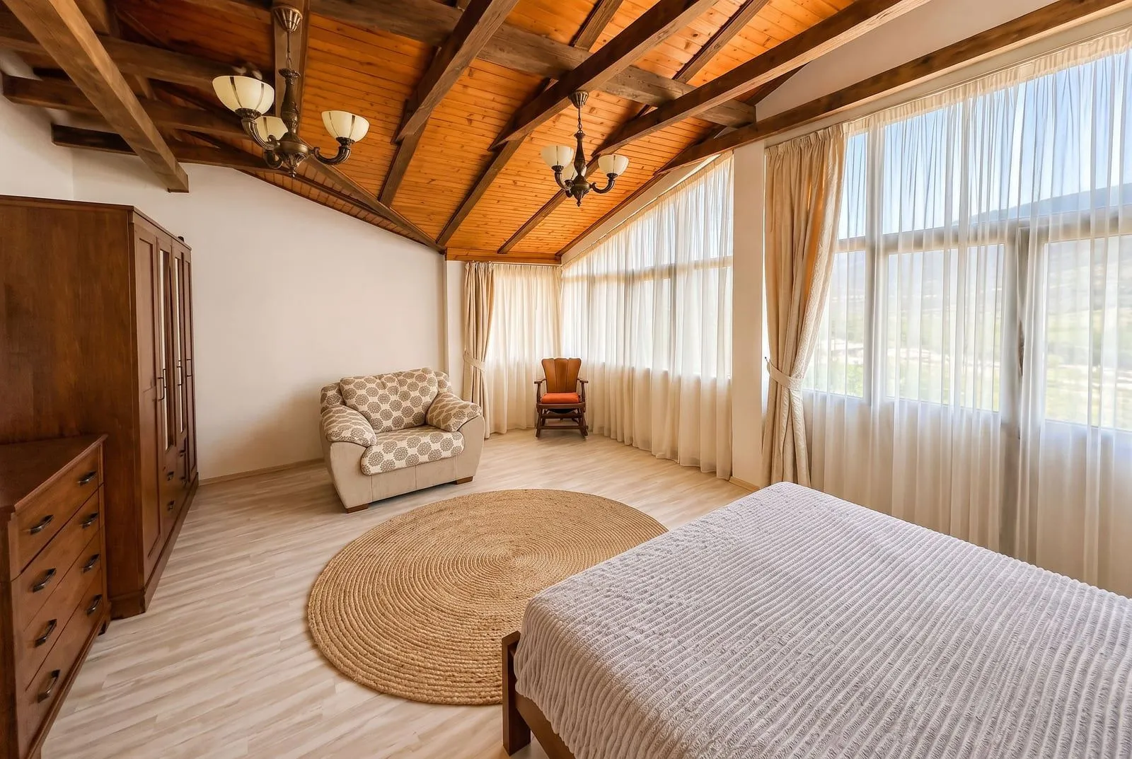 Spacious bedroom with wooden ceiling beams, a double bed and large windows.