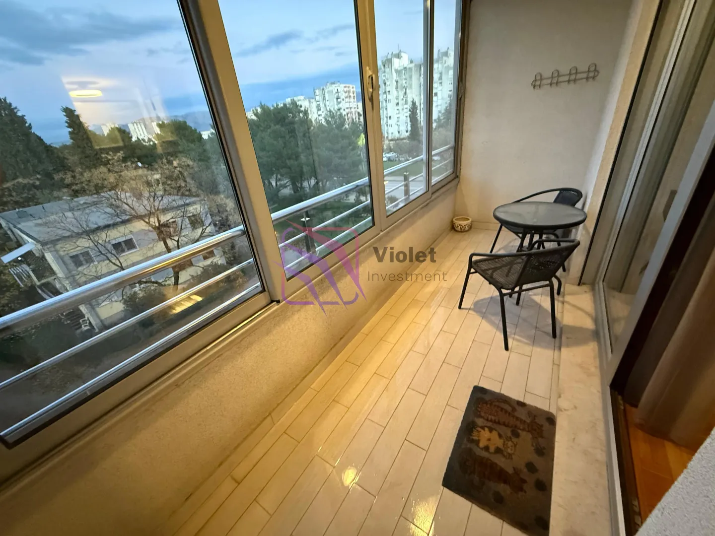 Zastakljeni balkon sa malim stolom, stolicama i pogledom na okolinu.