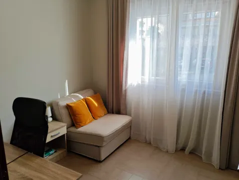 Small sofa with decorative pillows next to a window with curtains and a desk. - image 9