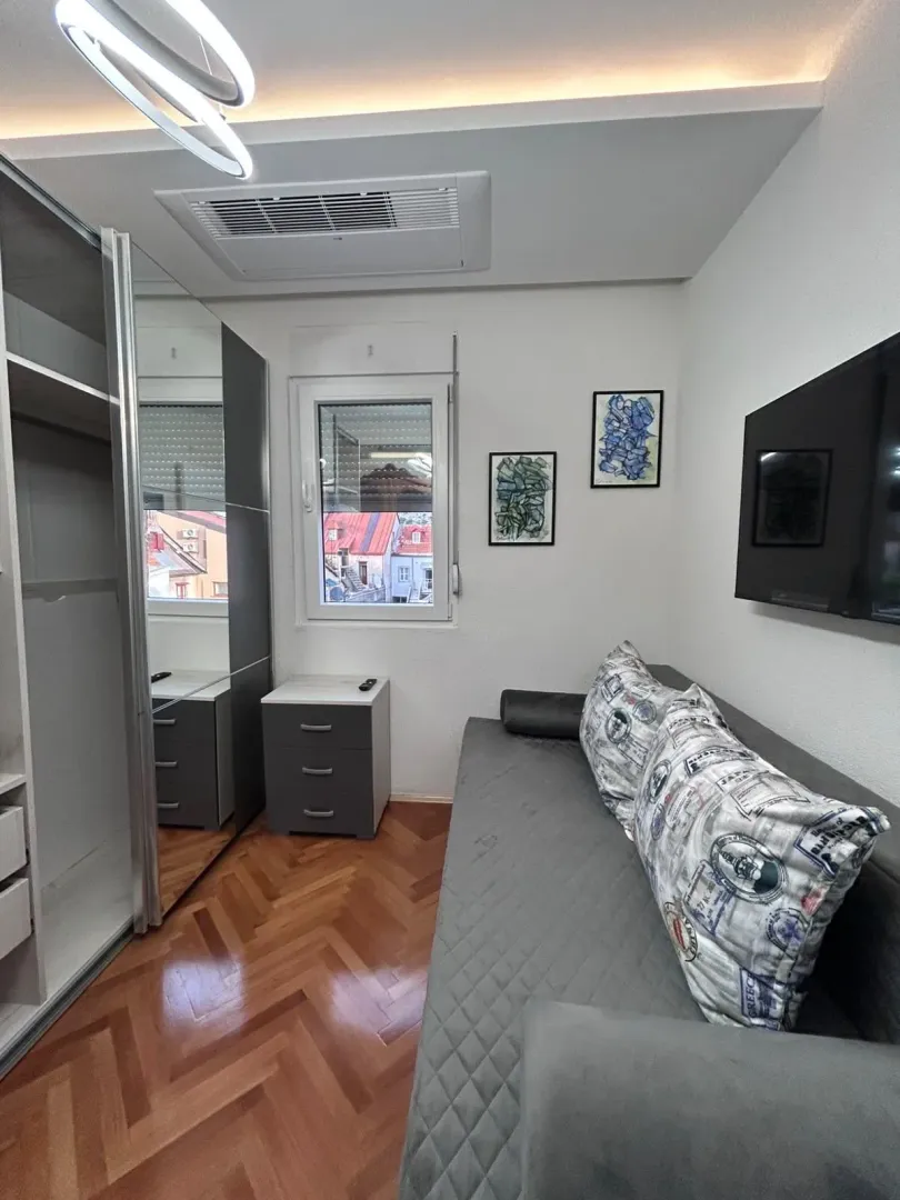 Small furnished bedroom with a sofa bed and a large wardrobe.