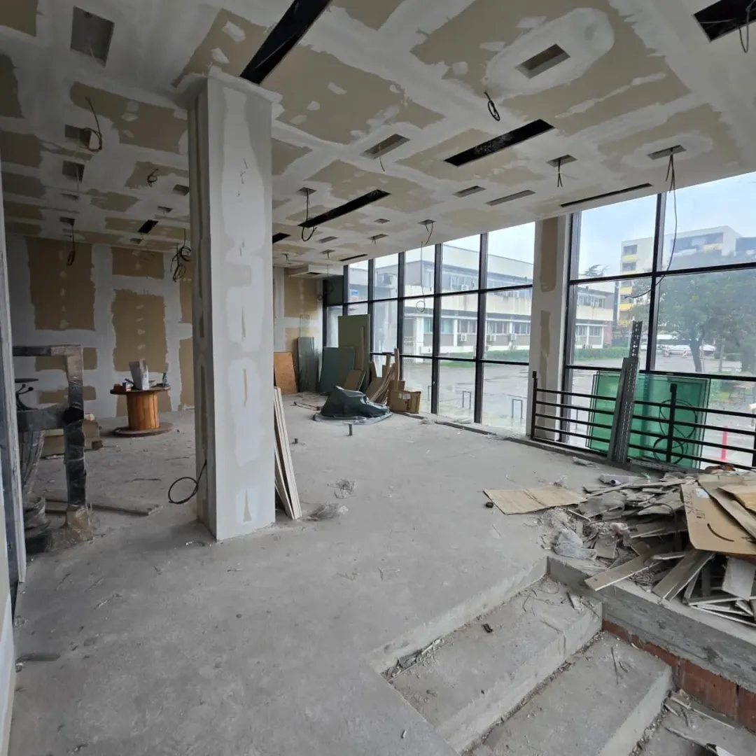 Large space under construction with large windows and construction materials.