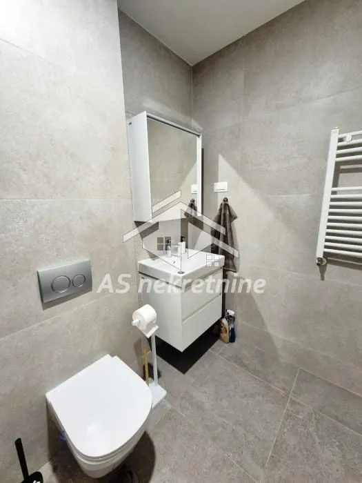 Modern bathroom with a washbasin, mirror, and toilet, tiled in grey.