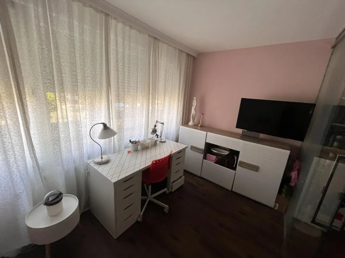 Radni sto sa stolicom i komodom sa televizorom u sobi sa velikim prozorom.