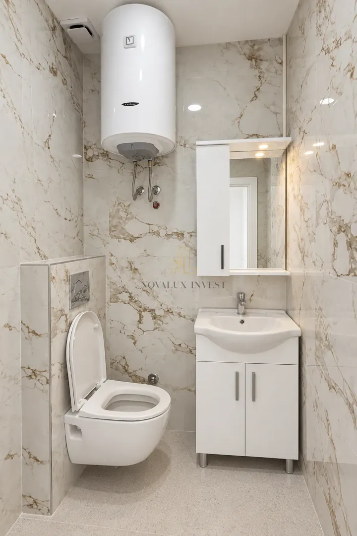 Bathroom equipped with a toilet, vanity unit with sink, mirror, and water heater.