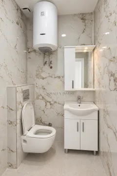 Bathroom equipped with a toilet, vanity unit with sink, mirror, and water heater. - image 6
