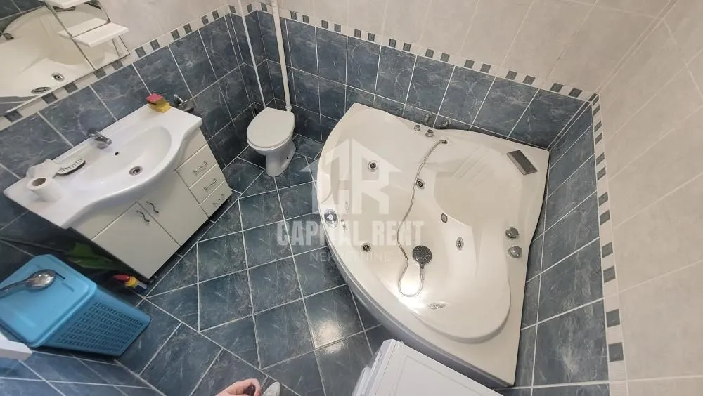 Kupatilo opremljeno umivaonikom, ugaonom kadom i toaletom sa pločicama u plavim tonovima.